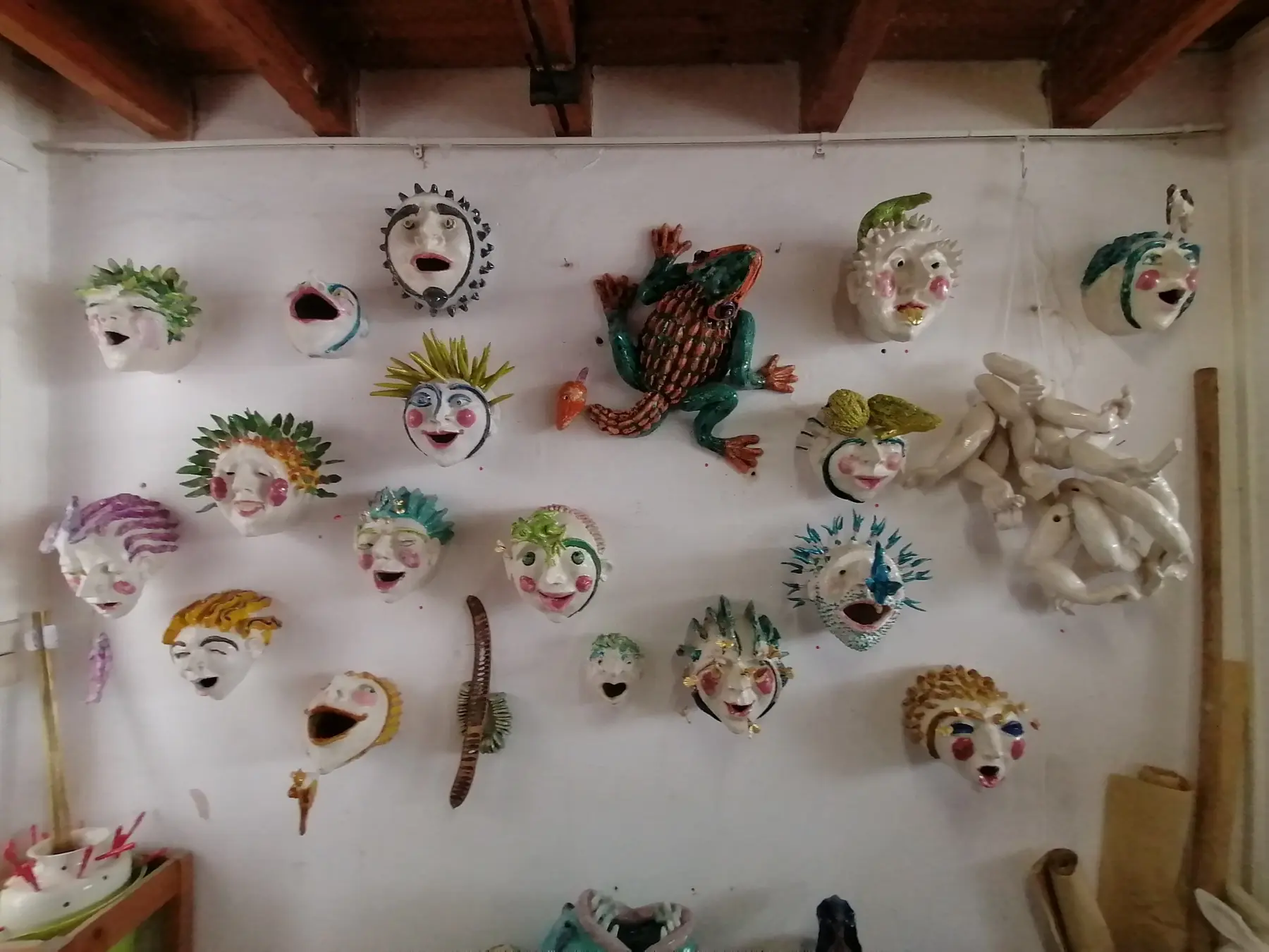 Playful glazed ceramic masks and creatures displayed on a studio wall