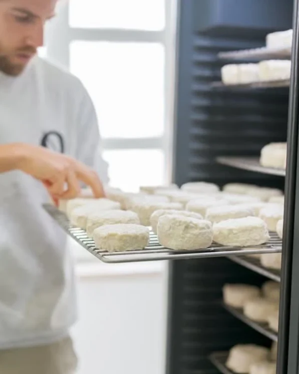 An artisan cheesemaker tending a tray of fresh cheeses
