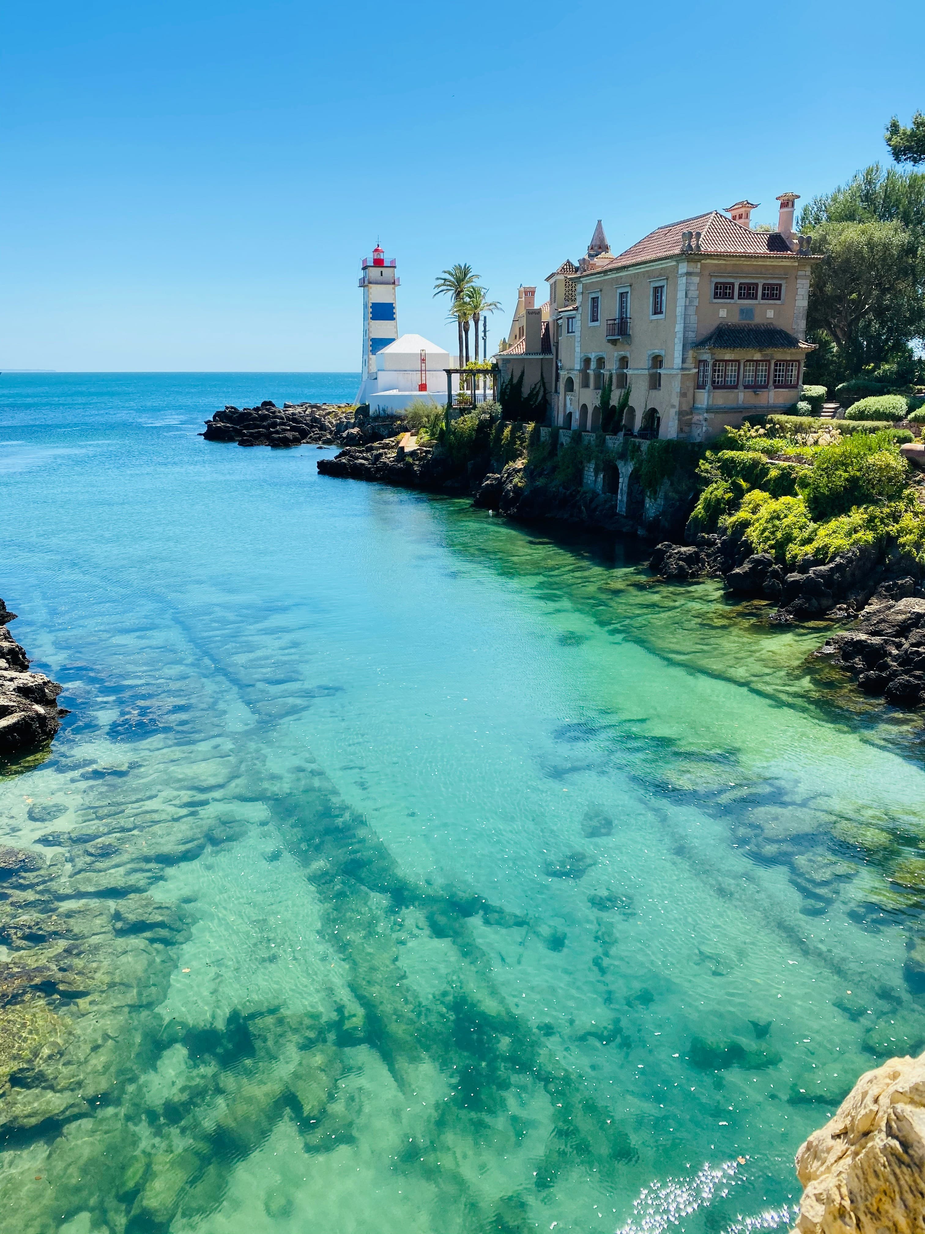 A lighthouse and historic house beside clear turquoise water