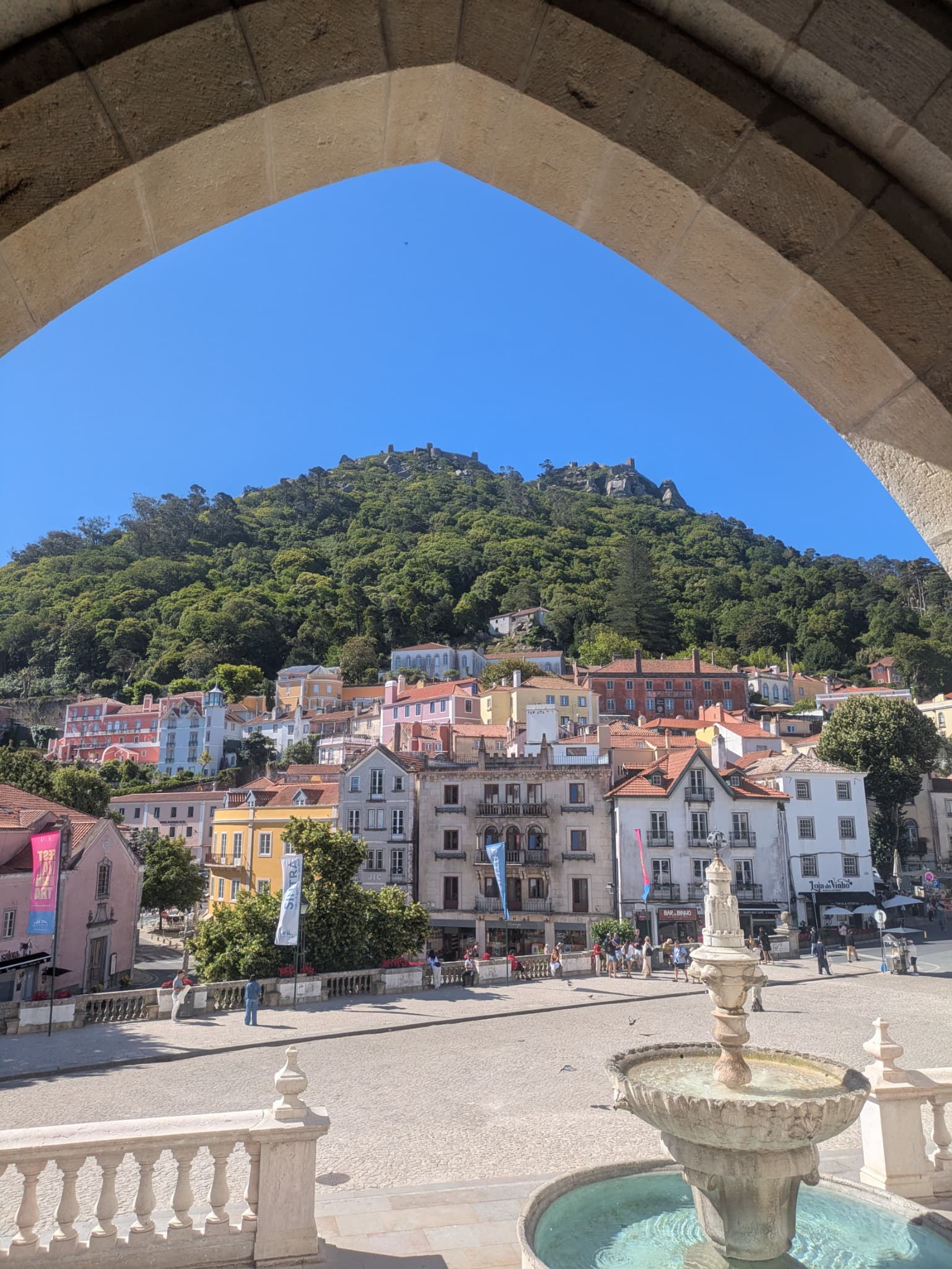 A view through a stone arch of Sintra's colourful village with the Moorish Castle on the hill behind